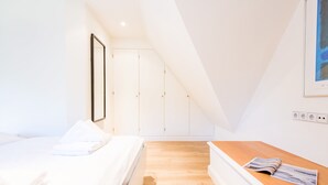 Une chambre à coucher avec un lit, une table de chevet en bois, une armoire blanche et une œuvre d’art encadrée accrochée au mur.