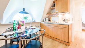 Une cuisine moderne avec des meubles en bois, un coin repas doté d’une table en verre et une grande verrière.