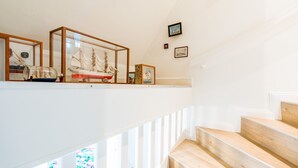 Un escalier avec des marches en bois et des rampes blanches, menant à un palier où sont exposés des objets maritimes encadrés.
