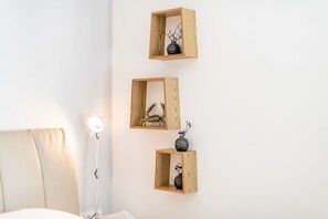 Three wooden wall shelves with decorative items, a bedside lamp, and a bed in a hotel room. - Terrasse. Zentral. Exklusiv (Westerland)