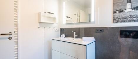 Une salle de bain moderne avec une douche à parois de verre, un meuble-lavabo blanc avec un miroir et une photographie en noir et blanc représentant un phare, accrochée au mur.