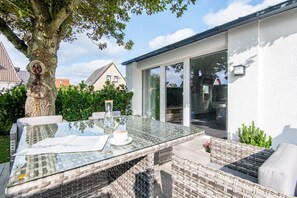 A glass-top table with wicker chairs, a white cup, and a glass pitcher in a garden setting. - Terrasse. Zentral. Exklusiv (Westerland)