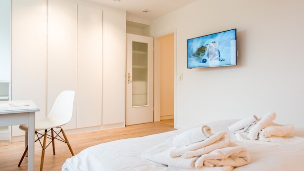 Una camera d'albergo con un letto, asciugamani bianchi, una scrivania, una sedia e un quadro appeso al muro.