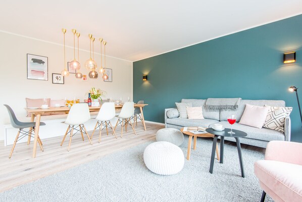 Uma sala de estar moderna com uma parede de destaque azul-turquesa, um sofá cinza e uma área de jantar com mesa e cadeiras de madeira.