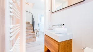 Un bagno moderno con lavandino bianco, mobile contenitore in legno e un grande specchio.