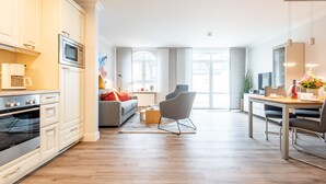 A modern kitchen with built-in appliances, a dining area with a wooden table and chairs, and a living space with a sofa and a coffee table. - Dachterrasse. Stimmig. Zentral. Residenz Bismarck, Whg. 17 Objekt-id: Hrb/17 (Westerland)