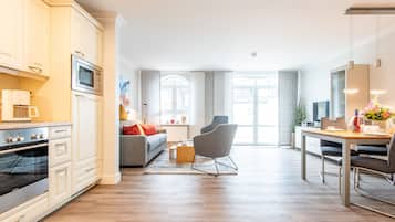 Eine moderne Küche mit eingebauten Geräten, ein Essbereich mit einem Holztisch und Stühlen sowie ein Wohnbereich mit Sofa und Couchtisch.