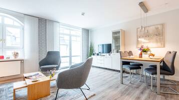 Un salon moderne avec une table basse en bois, un fauteuil gris et un coin repas comprenant une table en bois et des chaises en métal.