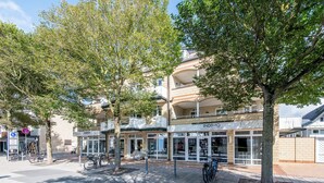 A building with a storefront, a bicycle parked outside, and a tree in front. - Dachterrasse. Stimmig. Zentral. Residenz Bismarck, Whg. 17 Objekt-id: Hrb/17 (Westerland)
