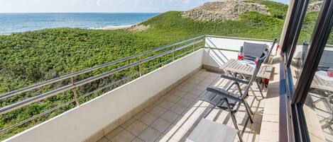 A balcony with a view of the ocean and a beach, furnished with chairs and a table.