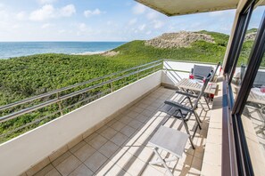 A balcony with a view of the ocean and a beach, furnished with chairs and a table.