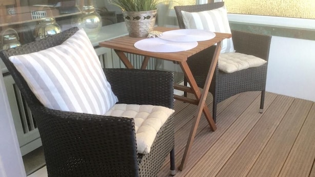 A wooden deck with wicker chairs and a table, a potted plant, and a window with a view. - Exklusiv. Zentral. Strandnah (Westerland)