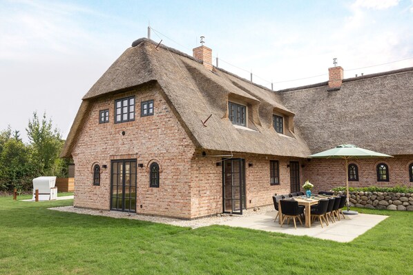 A brick house with a thatched roof, a patio with a table and chairs, and a covered outdoor seating area.
