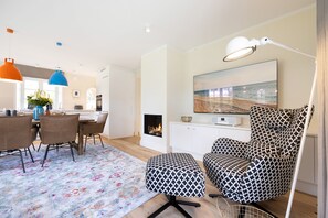A modern living room with a fireplace, a dining area with a table and chairs, and a patterned rug.