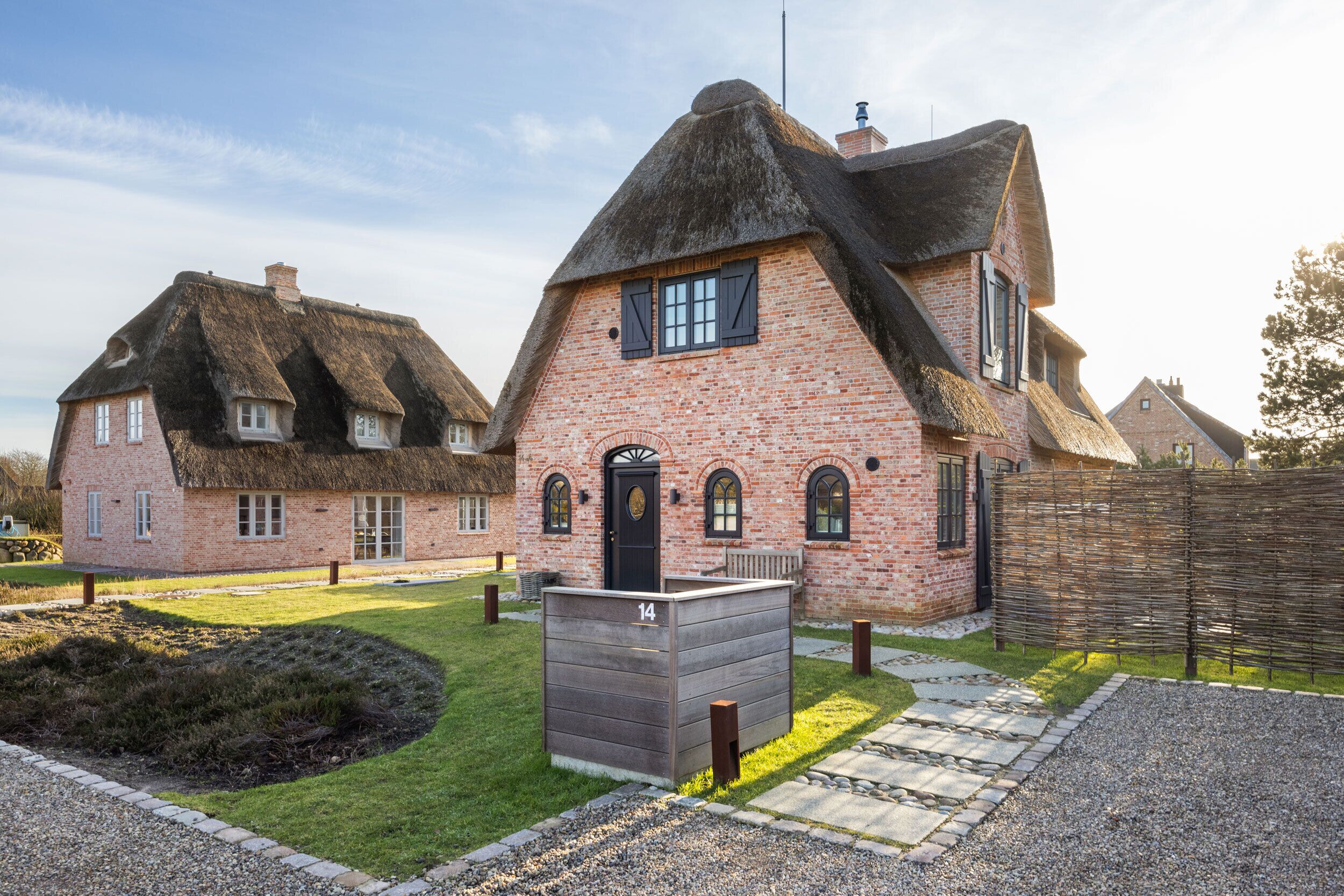 Ein traditionelles Backsteinhhaus mit einem Reetdach, ein kleiner Holzschuppen und ein gepflegter Rasen.