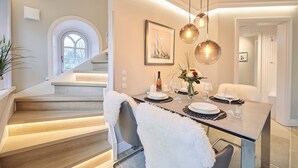 Un coin repas avec une table moderne dressée pour quatre personnes, un escalier agrémenté d’un fauteuil blanc moelleux et un tableau encadré accroché au mur.