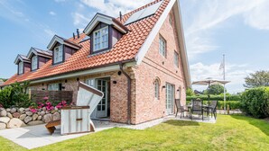 Una casa de dos pisos con techo de tejas rojas, fachada de ladrillo y un patio con mobiliario exterior.