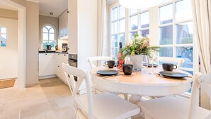 Una cocina moderna con armarios blancos, una mesa redonda de comedor con sillas blancas y un ventanal con cortinas.