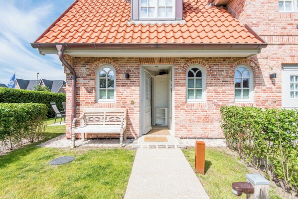 A brick house with a red-tiled roof, a front porch with a bench, and a door leading to the interior.