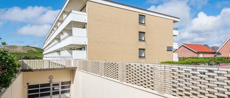 Un immeuble moderne à plusieurs étages, doté d’un toit plat, d’une façade en briques et d’une entrée sécurisée par un portail.