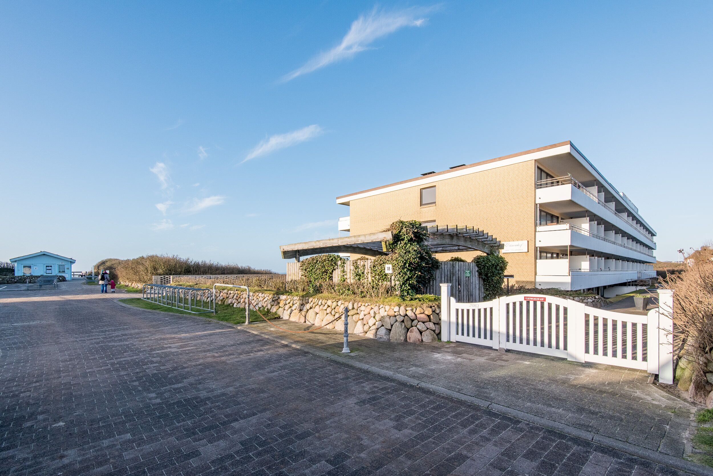 A modern multi-story building with a flat roof and a stone wall.