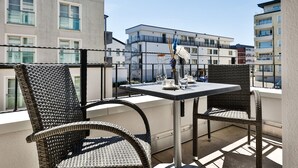 Un balcón con sillas de mimbre y una mesa, con vista a un paisaje urbano con edificios modernos.