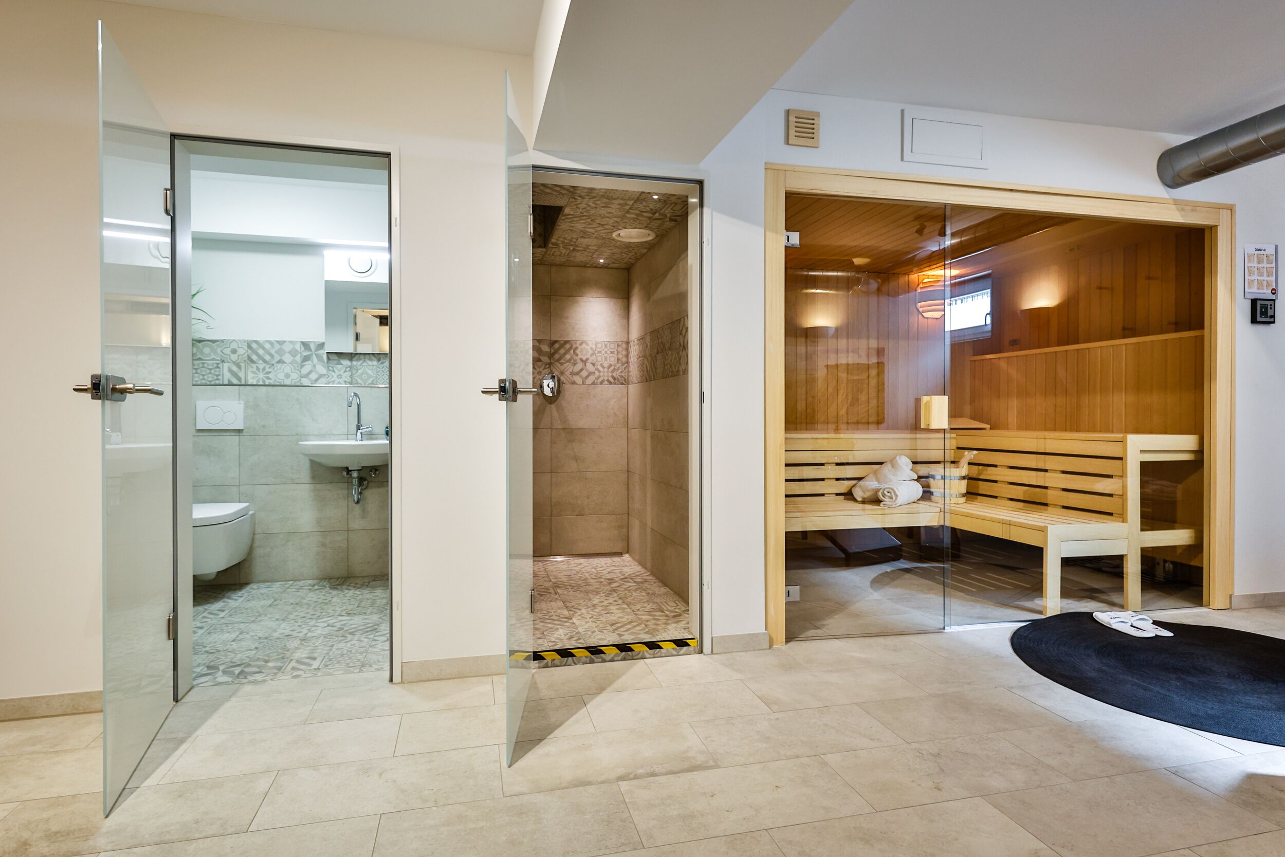 A modern bathroom with a glass shower enclosure, a wooden sauna, and a bench with towels.