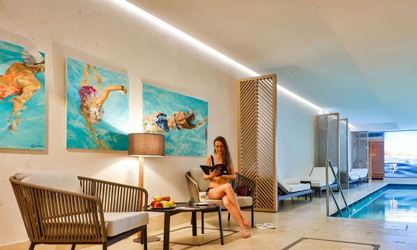 A modern hotel lobby with a pool area, featuring artwork, seating, and a view of the pool.