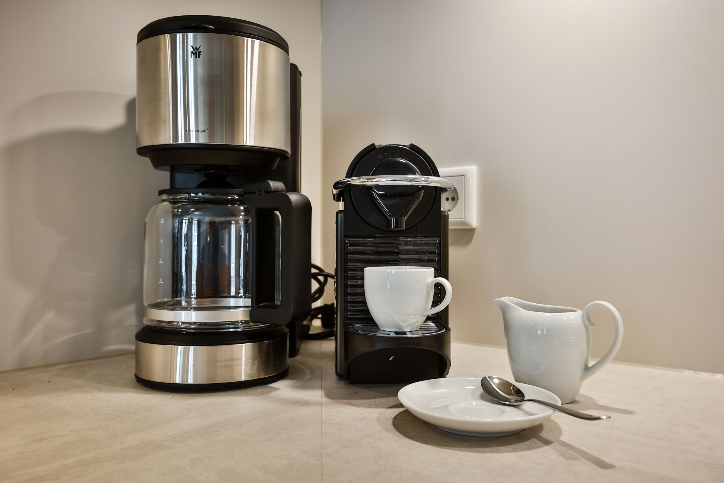 Eine Kaffeemaschine, eine Tasse und eine Kanne auf einer Arbeitsplatte.