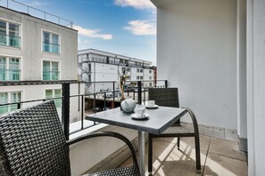 Ein Balkon mit Korbstühlen und einem Tisch, mit Blick auf eine Stadtlandschaft mit Gebäuden und blauem Himmel.