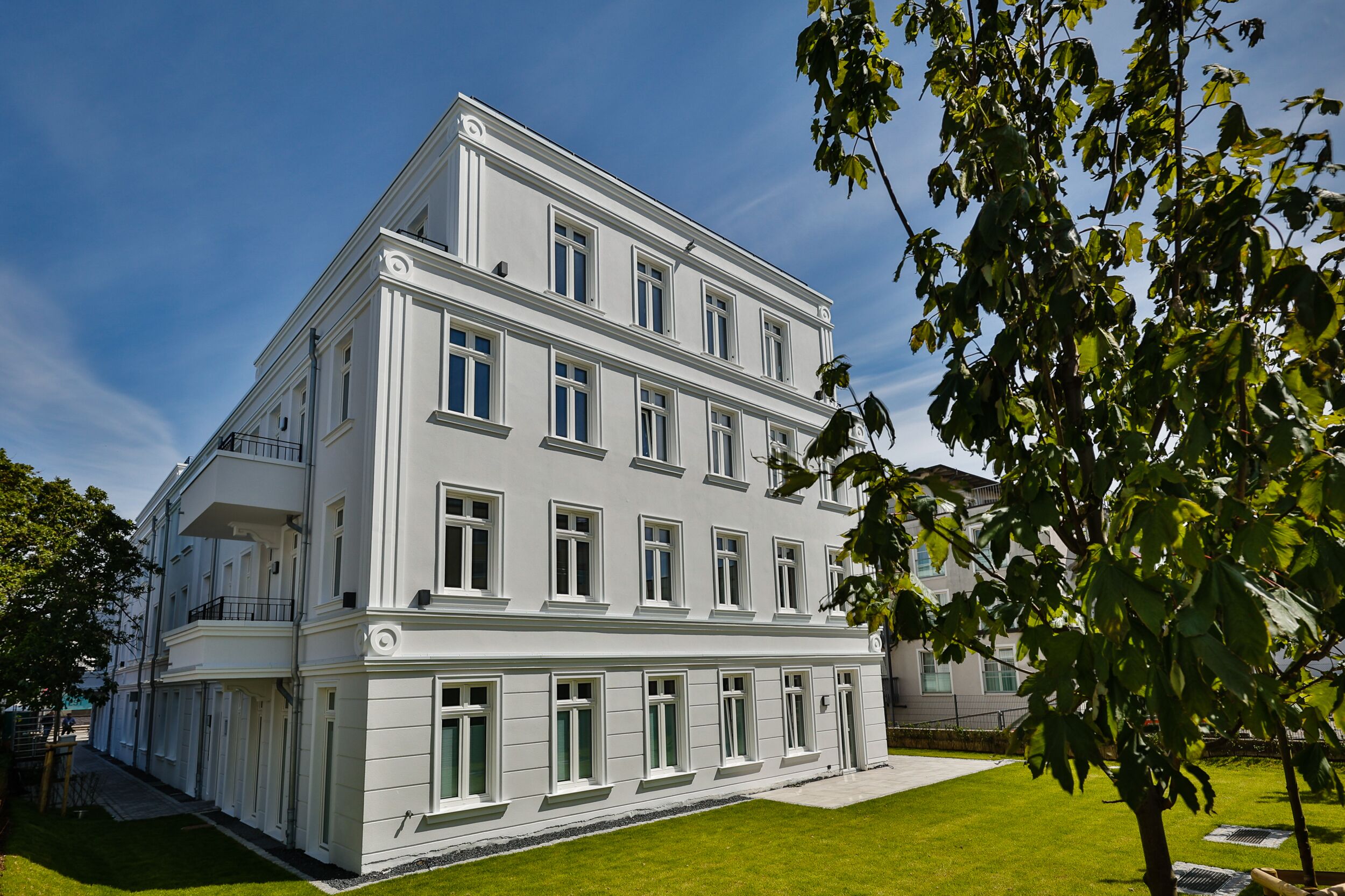 A multi-story building with a symmetrical facade, large windows, and a well-maintained lawn.