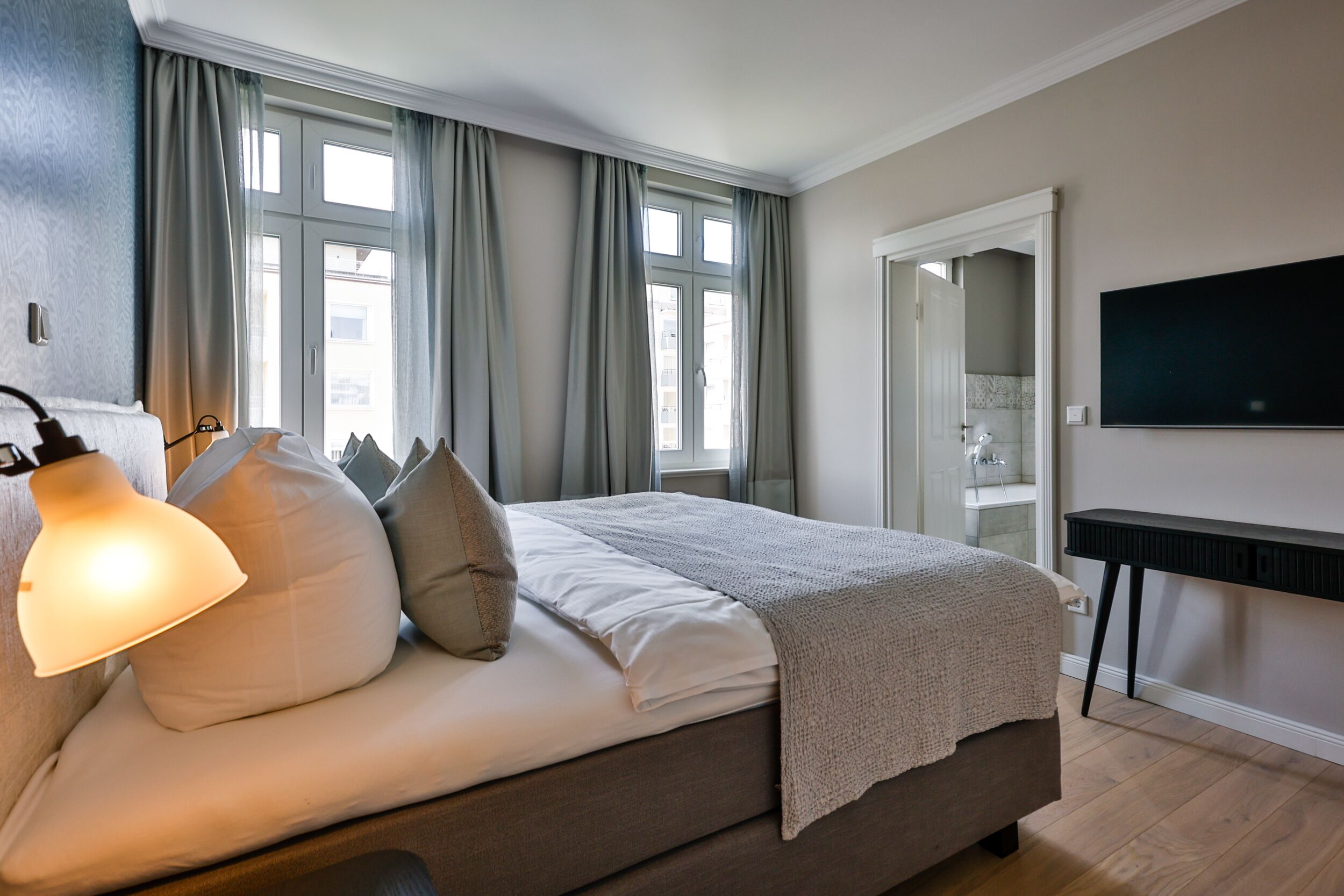 Une chambre à coucher avec un lit, une lampe de chevet, une télévision et une fenêtre avec des rideaux.