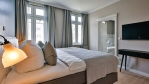 A bedroom with a bed, a bedside lamp, a TV, and a window with curtains.