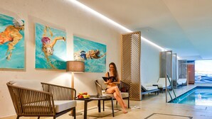 A modern indoor pool area with lounge chairs, a table with fruits, and artwork on the walls.