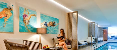 Un área interior de piscina moderna con sillones de descanso, una mesa con frutas y obras de arte en las paredes.