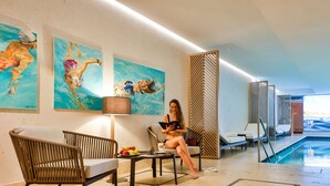 Un área junto a la piscina con sillones de descanso, una mesa con fruta y obras de arte en las paredes.
