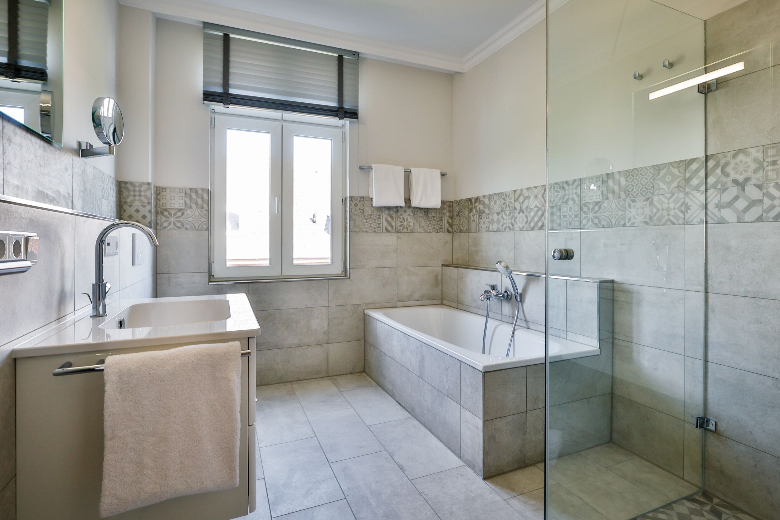 Ein modernes Badezimmer mit Badewanne, einer Glasdusche und einem Waschbecken mit Spiegel.