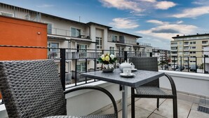 A balcony with wicker furniture, a table, and a vase of flowers. - Neubau. Strandnah. Anspruchsvoll. Objekt-id: Ljw/14 (Westerland)