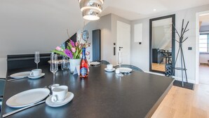 A modern dining area with a dark table set for four, including plates, cutlery, and a bottle of wine.