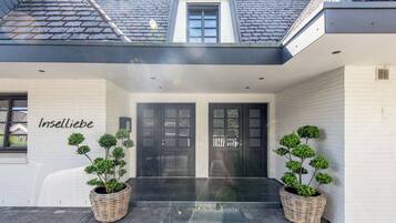 A modern building with two large black doors, a small window above the doors, and two large wicker planters with small trees.