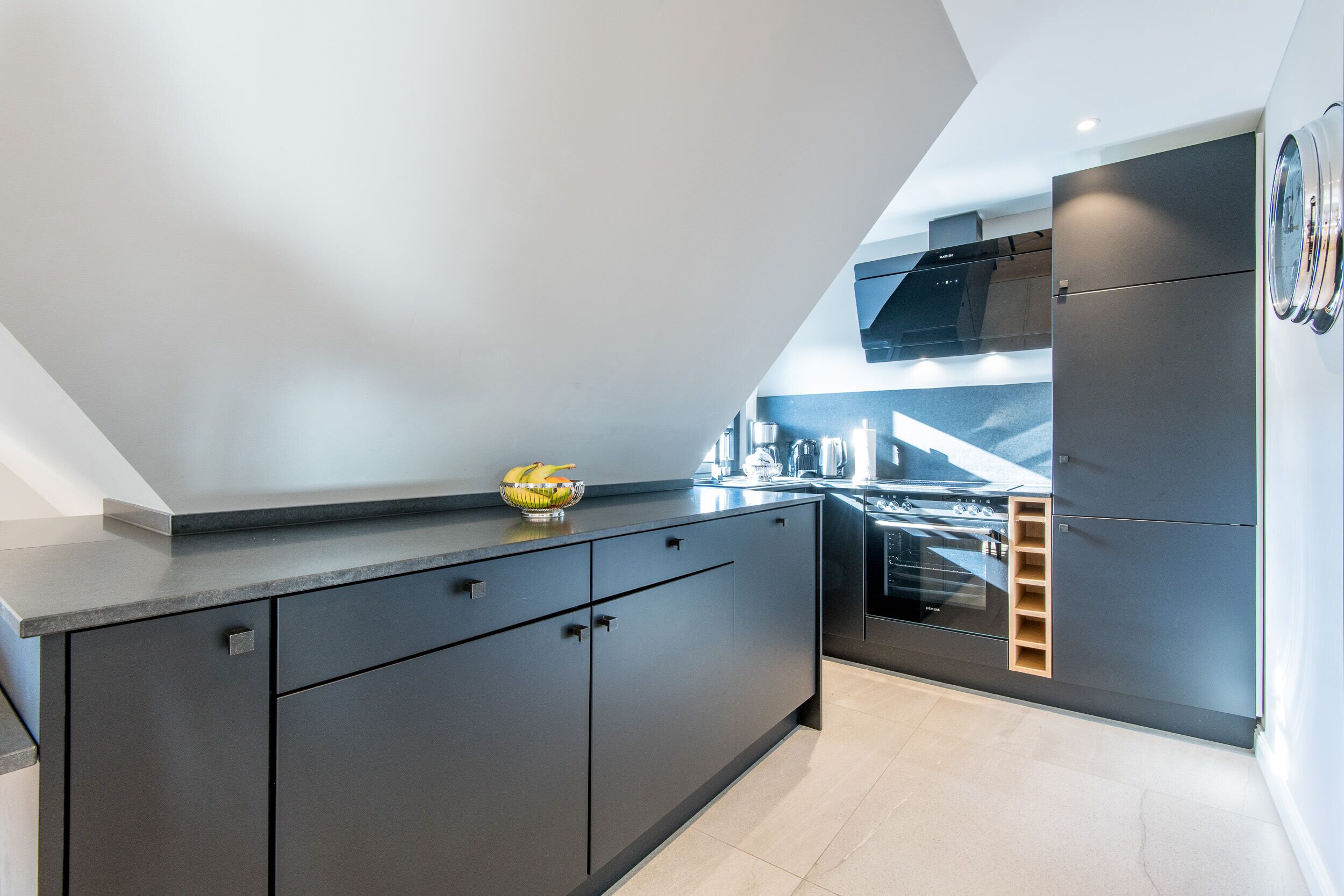 A modern kitchen with dark cabinetry, a built-in oven, and a stainless steel range hood.