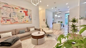 A modern living room with a large abstract painting, a sofa set, a coffee table, and a dining area with chairs and a small island. - Lovely stylish suite in a historical Brooklyn area (Brooklyn)