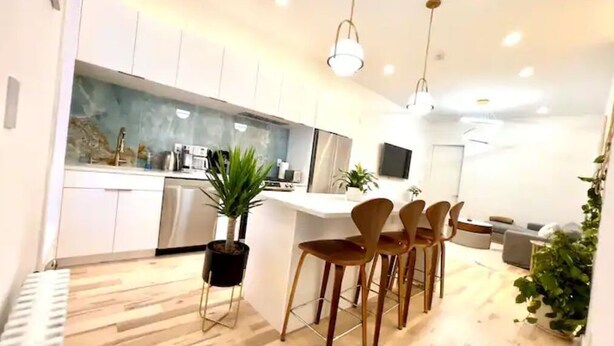 A modern kitchen with white cabinets, a central island, and bar stools. - Lovely stylish suite in a historical Brooklyn area (Brooklyn)