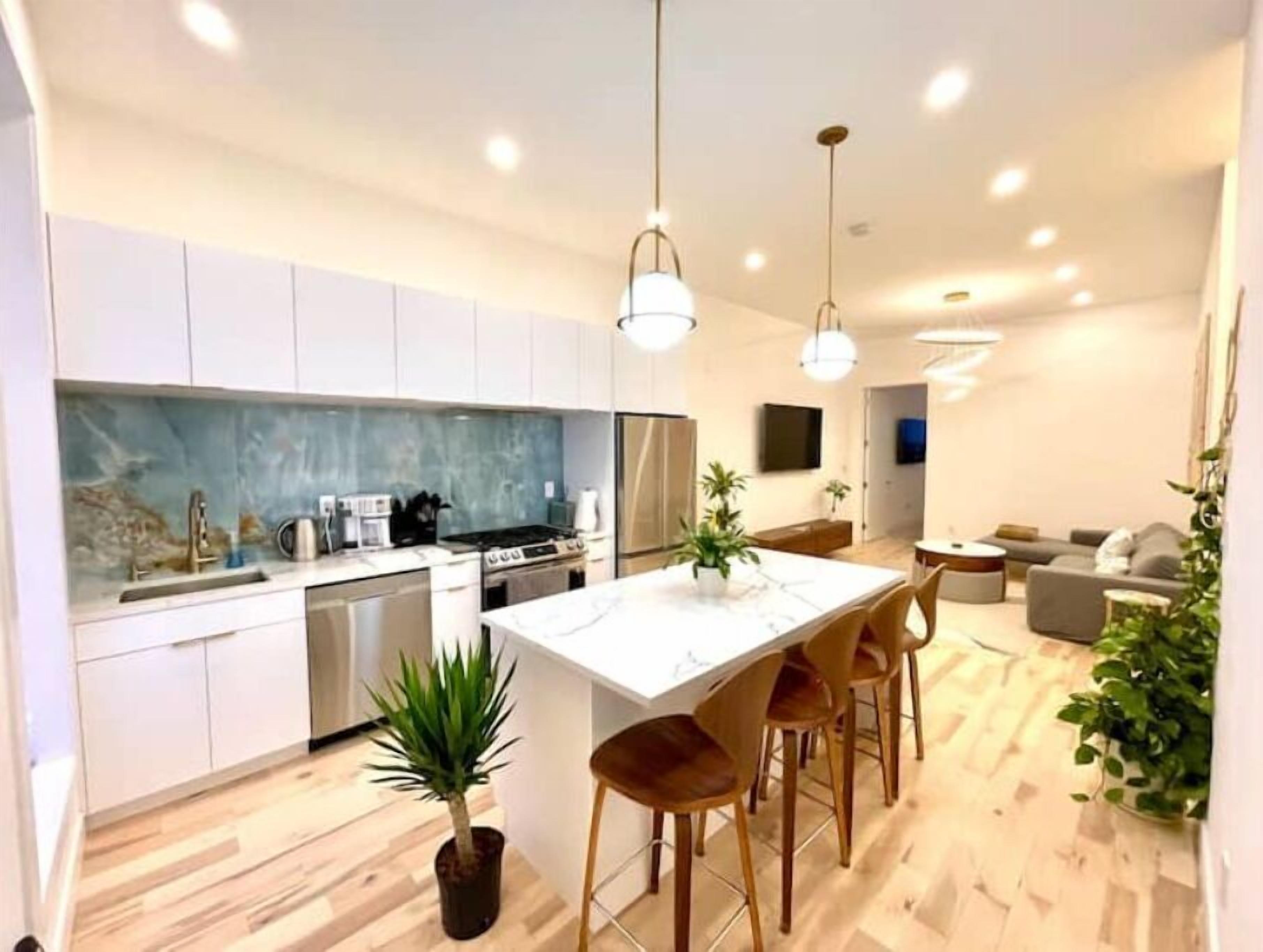 Une cuisine moderne avec des meubles blancs, un îlot central et des luminaires suspendus.