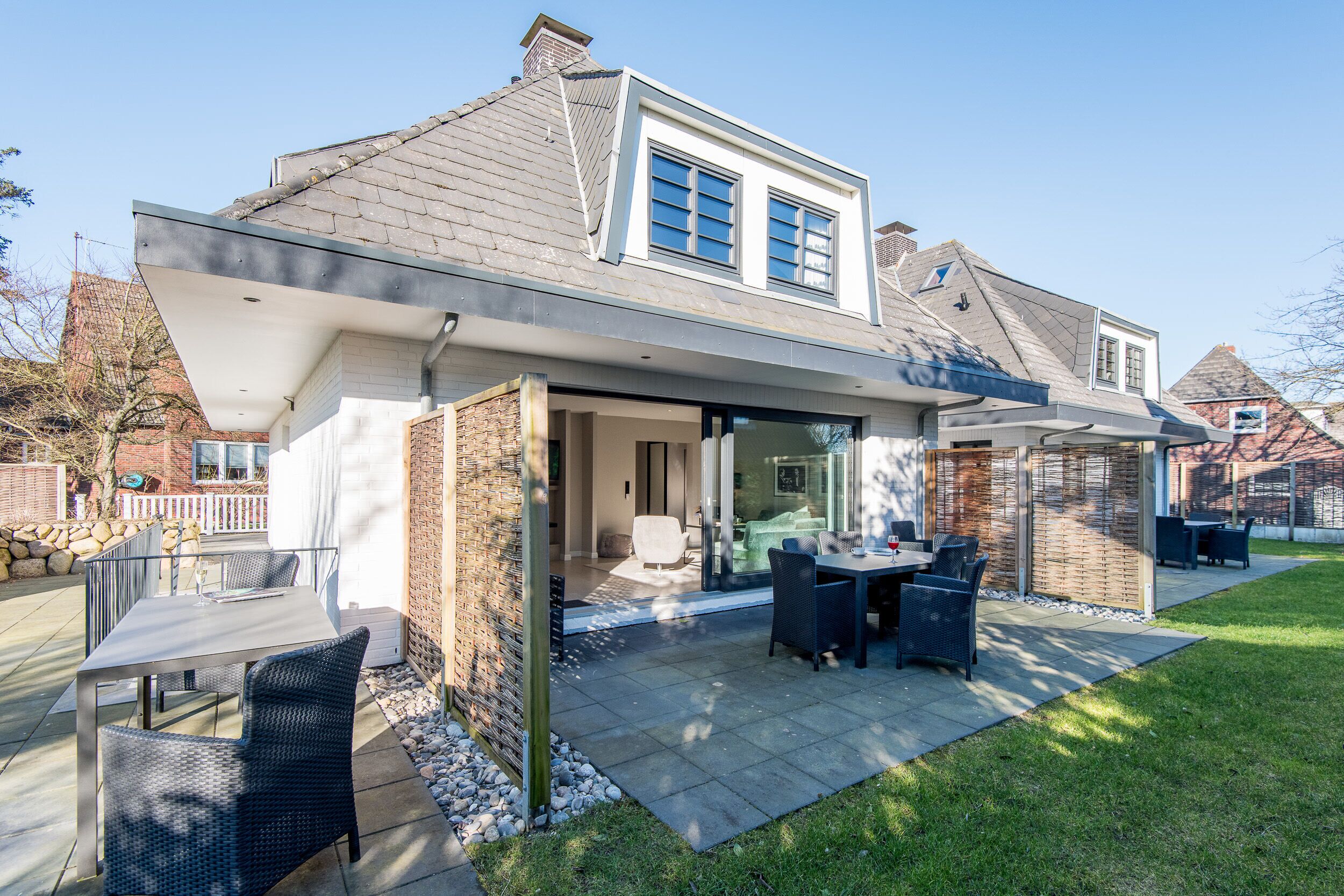Ein modernes Haus mit überdachter Terrasse, Außenmöbeln und einer Ziegelhausfassade.