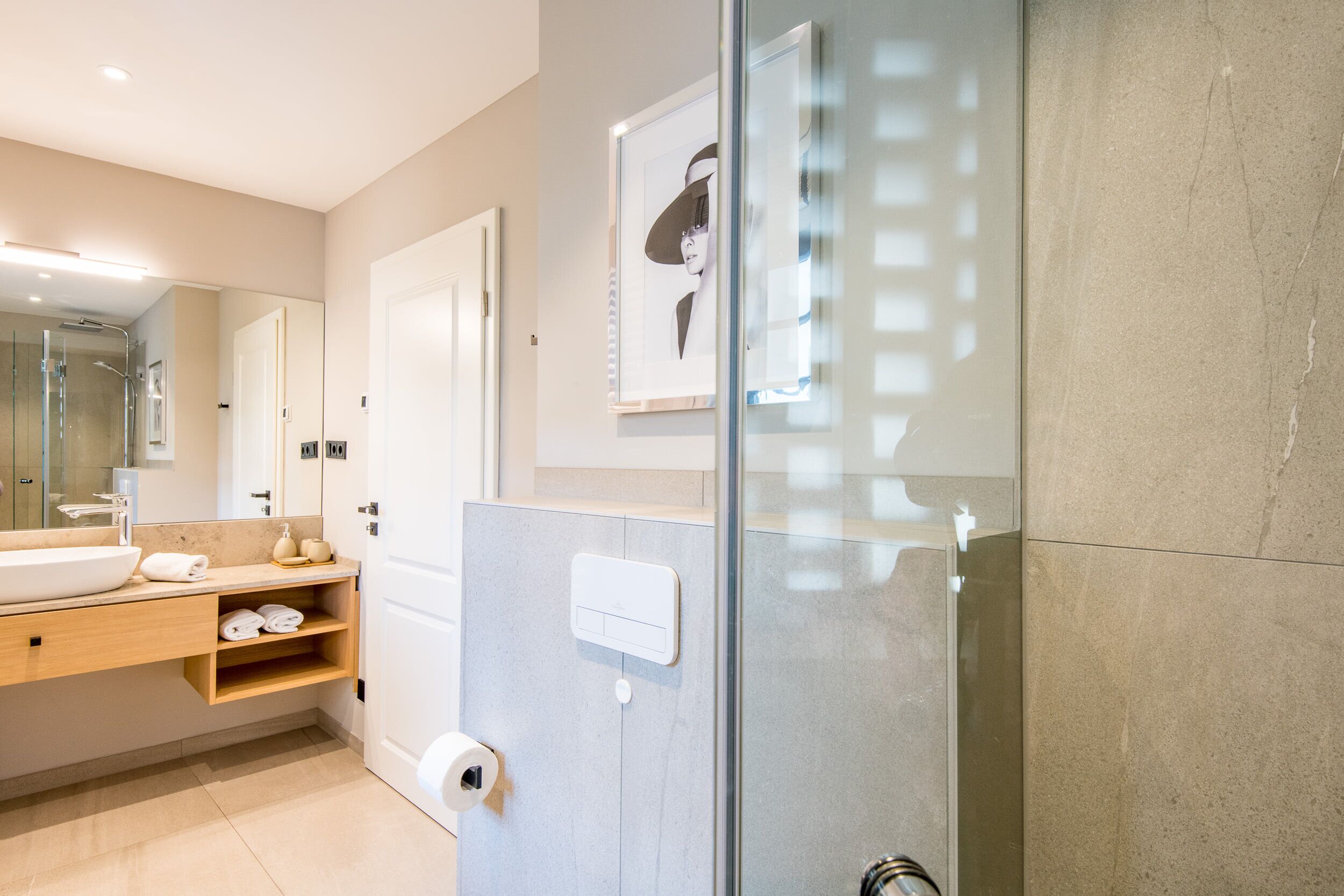 A modern bathroom with a glass shower enclosure, a large mirror, a sink, and a towel rack.