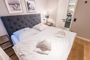 A neatly made bed with white linens and towels, a tufted headboard, and a small bedside table with a lamp.