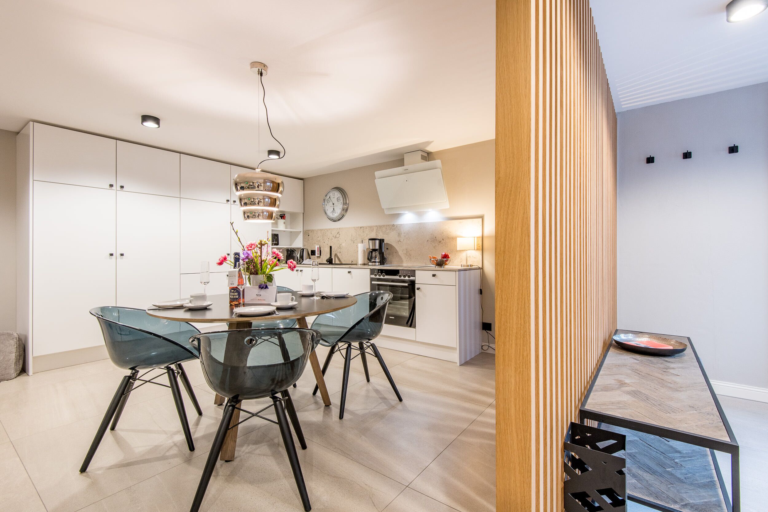 A modern kitchen with white cabinets, a built-in oven, and a dining area with a glass table and chairs.