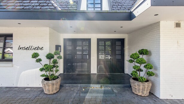 A modern building with two large black doors, a small window above the doors, and two large wicker planters with small trees.