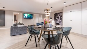 A modern dining area with a round table, clear glass chairs, and a chandelier.